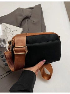 Minimalist black double-zipper crossbody bag with broad brown strap and gold hardware