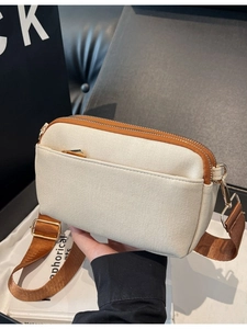 Beige canvas crossbody bag with brown leather trim and triple-zipper compartments