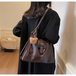 Detail einer dunkelbraunen Ledertasche mit Vintage-Schnalle und Plüschbär-Anhänger
