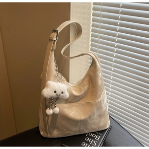 Detail of beige glossy hobo bag with cloud texture and cute white plush charm accessory