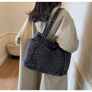Détail d'un sac cabas en denim bleu foncé avec poches porté sur un manteau beige