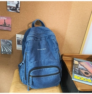 Detalle de mochila vintage de mezclilla azul con bordado blanco sobre banco de madera
