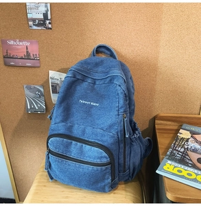Detalle de la mochila de mezclilla lavada con bordado blanco y bolsillo lateral en silla de madera