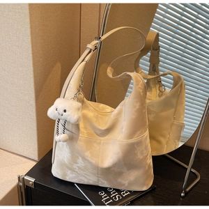 Detail of beige tote bag with wide shoulder strap and white cloud plush pendant