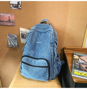 Detalle de mochila vaquera azul claro con bordado 7street blanc en un banco de madera