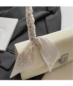 Dettaglio di twilly in seta con motivo a reticolo di cuori legato al manico di una borsa