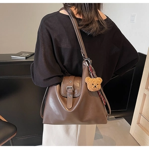 Detail der dunkelbraunen Leder-Tote-Bag mit Schnalle und Bärenanhänger an einem Model