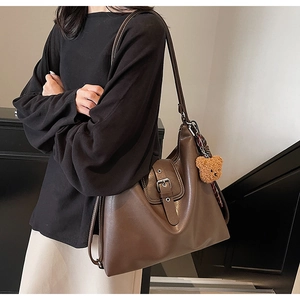 Detail der dunkelbraunen matten Ledertasche mit Silberschnalle und Plüschbär-Anhänger