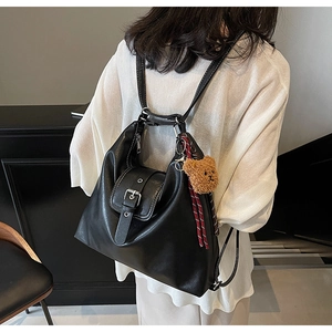 Detail eines schwarzen Vintage-Rucksacks mit Deko-Schnalle und Plüschbär-Anhänger