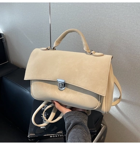 Detail of a beige matte leather handbag with metallic buckle and top handle