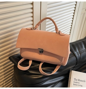 Detail view of pink matte leather backpack with metal buckle and top handle on dark base