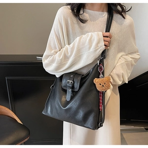 Detail der schwarzen Ledertasche mit weißen Nähten und süßem Bären-Anhänger