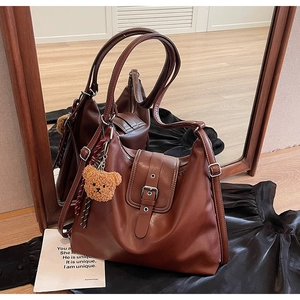 Detail der braunen Vintage-Ledertasche mit Metallschnalle und Plüschbär-Anhänger