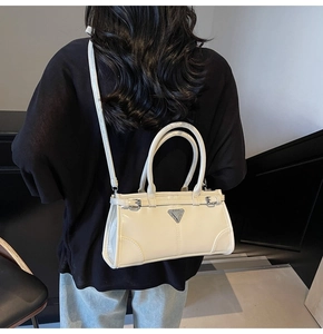 Detail of white glossy crossbody bag featuring silver triangle logo and metal buckles