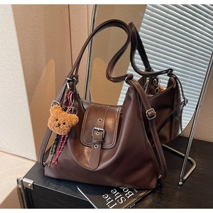 Detailansicht der dunkelbraunen Ledertasche mit Zierschnalle und Plüschbär-Anhänger