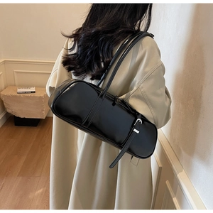 Detail of a black glossy baguette bag with adjustable strap worn by a model in a beige coat