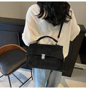 Detail of black frosted messenger bag showing silver metal buckle and matte texture
