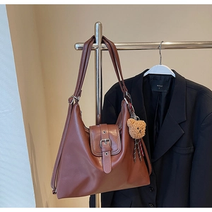 Details einer braunen Tragetasche mit Zierschnalle und Plüschbär-Anhänger auf Metallständer