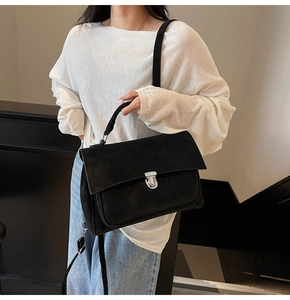 Detail of black matte leather satchel with silver buckle worn by a model in casual style