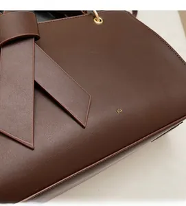 Detail einer dunkelbraunen Ledertasche mit seitlicher Schleife und Goldakzenten
