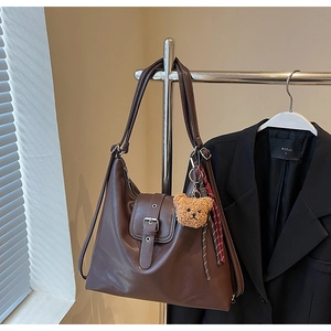 Detail der dunkelbraunen Kunstleder-Tasche mit Silberösen und einem Plüschbär-Anhänger