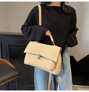 Detail view of beige matte messenger bag with metal buckle and top handle worn by a model