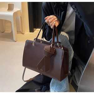 Detail einer dunkelbraunen Ledertasche mit Knotendesign und goldfarbenen Beschlägen