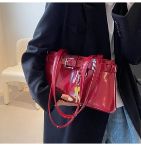Detail of red patent leather baguette bag with belt buckles and key pendant charm