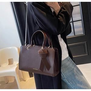 Detail einer dunkelbraunen Tote Bag mit dekorativem Knoten und goldenem Logo-Schriftzug