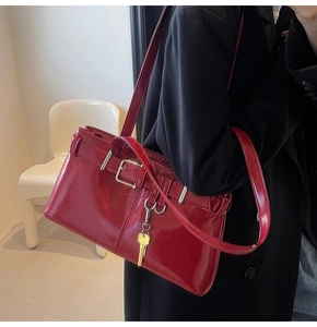 Detail of glossy deep red patent leather shoulder bag with silver buckle and gold key charm