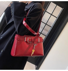 Detail of red glossy shoulder bag with gold key charm and strap buckle on a black blazer