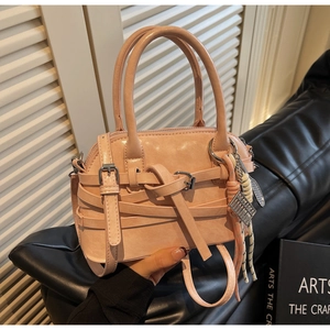 Pink shell handbag detail with decorative straps, metal buckles and colorful charms