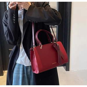 Detail einer weinroten Ledertasche mit Goldlogo und Schleifenanhänger an einem Model