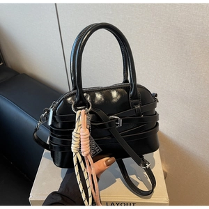 Detail of black patent leather shell bag with woven rope charm and top handles