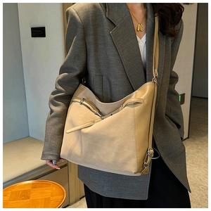 Detail of large beige shoulder bag with textured patchwork panels and metal buckles
