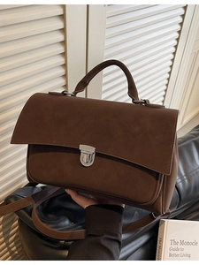 Deep brown matte messenger bag with top handle and silver buckle on chic office backdrop