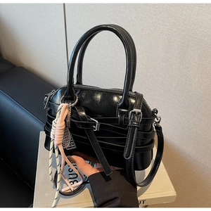 Detailed shot of a black glossy leather shell bag with unique tiered buckle straps
