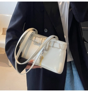 Detail view of a white glossy leather shoulder bag with a metal key charm and buckle strap