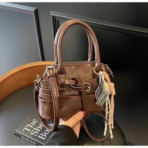 Close-up of brown patent leather handbag with decorative straps and racket charm