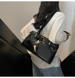 Detail of glossy black shoulder bag with silver buckles and yellow key charm