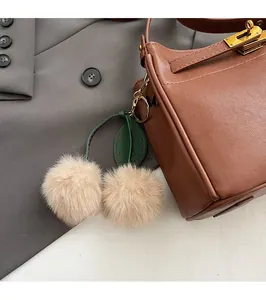 Close-up of brown litchi leather bag featuring a cute cherry plush charm and gold metal lock