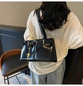 Detail of black glossy vintage shoulder bag featuring metallic buckle and key charm