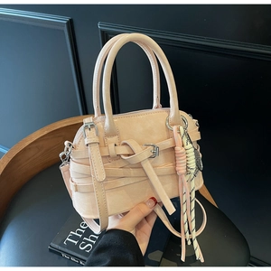 Detail of apricot shell shoulder bag with woven strap design and decorative tassel charm