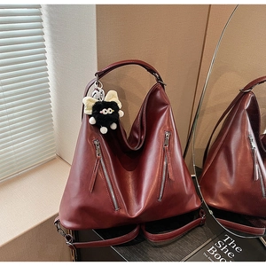 Detail view of deep red leather shoulder bag featuring decorative zippers and a plush charm