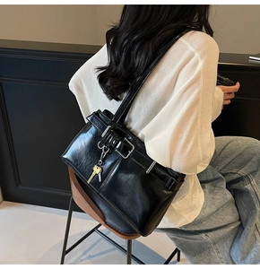 Detail of glossy black shoulder bag featuring silver buckle and key pendant accessory