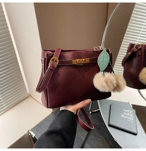 Detail of burgundy handbag with cherry plush charm and golden lock on leather surface