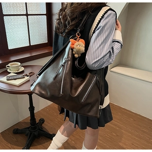 Detail of dark brown leather tote bag with dual zipper accents and plush charm