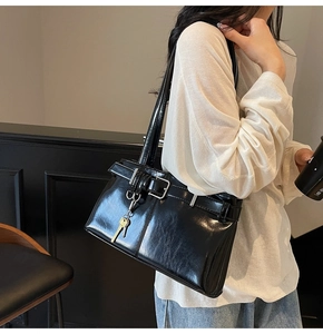 Detail of black glossy handbag featuring gold key charm and decorative leather strap buckles