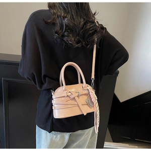 Close-up of pink shell bag with cross strap buckle, silver charm, and plaid scarf detail