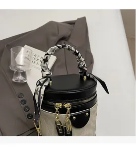 Detail of beige canvas cylinder bag with black leather flap and silk scarf handle